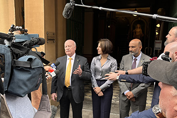 Three people stand outside court, being interviewed by journalists.